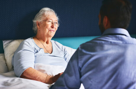 Happy senior female patient lying on bed with doctor comforting her at nursing home